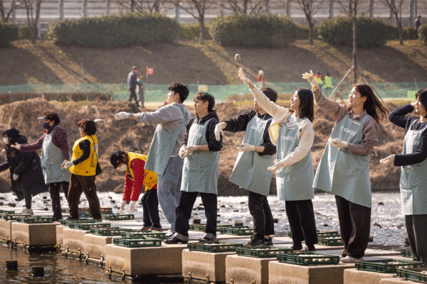 코웨이 임직원 봉사자들이 2025년 3월 21일 제4회 EM 흙공 던지기 봉사활동 중 서울 금천구 안양천 다리에서 EM 흙공을 던지고 있다. /코웨이