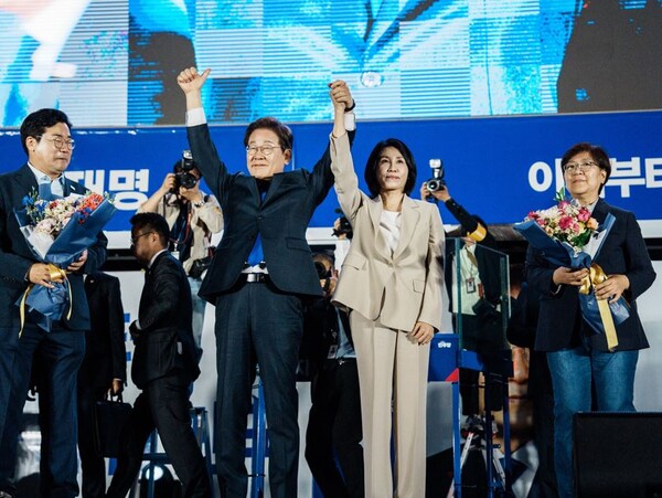 제21대 대통령 당선이 확실시되는 더불어민주당 이재명 대선 후보와 부인 김혜경 여사가 4일 서울 여의도 국회 인근에서 당 주최로 열린 국민개표방송 행사에 참석해 박찬대 상임총괄선대위원장과 정은경 총괄선대위원장단으로부터 꽃다발을 받은 뒤 시민들을 향해 두 팔을 들어 인사하고 있다. 2025.6.4 공동취재연합