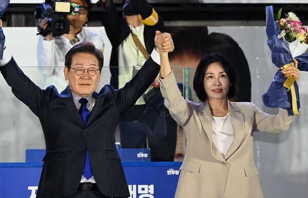 이재명 제21대 대통령과 부인 김혜경 여사가 2025년 6월 4일 서울 여의도 국회 인근에서 당 주최로 열린 국민개표방송 행사에 참석해 꽃다발을 받고서 시민들을 향해 두 팔을 들어올려 인사하고 있다./연합