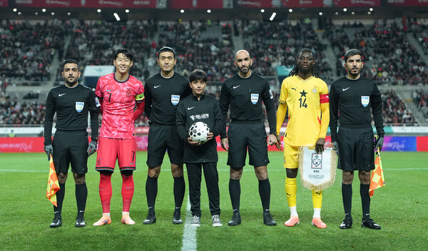 하나은행은 2025년 11월 18일 서울월드컵경기장에서 열린 대한민국과 가나의 축구 국가대표팀 A매치 경기에서 이주배경 가정 아동·청소년들에게 '매치볼 키드'와 '기수단'으로 참여할 수 있는 특별한 체험 기회를 제공했다. 경기 시작에 앞서 아프가니스탄 출신 매치볼 키드 마시(Masih)가 양 팀 주장 및 심판진과 기념촬영을 하고 있다./사진=하나은행